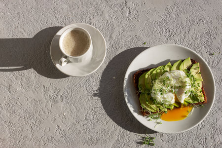 Healthy breakfast on a sunny morning, toasted whole grain bread with avocado, poached egg, microgreens and a cup of coffee. Place for your text.の写真素材