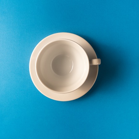 Flat lay view of the one white empty coffee or tea cup on blue color background, closeup, copy space.の写真素材