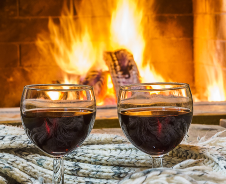 Red wine  in a glasses  with  wool things,  before cozy fireplace background,  in country house, christmas  winter vacation.の写真素材