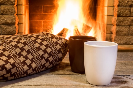 Two cups for hot tea or coffee and cozy warm scarf near fireplace, in country house, winter vacation, horizontal.の写真素材