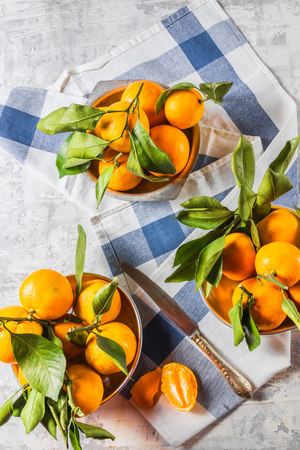 Flat lay view of Orange ripe mandarins fruit with green leaves, in bowls, on a blue and white napkin, over rustic white wooden background, vertical, copy space.の写真素材