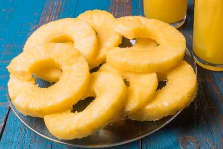Low angle view of two glasses of pineapple juice and a plate with pieces of pineapple fruit over old blue wooden backgroundの写真素材