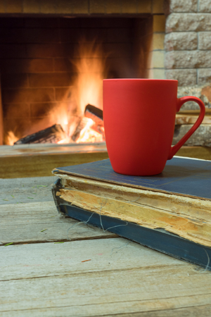 Red mug with tea, and a book , near cozy fireplace, in country house, winter vacation, vertical orientation.の写真素材