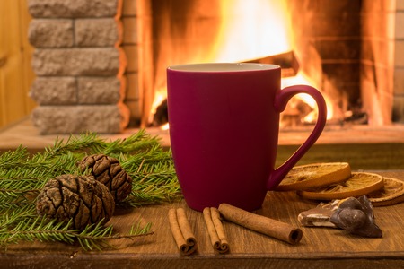Merry Christmas near cozy fireplace, with mug of hot drink, cinnamon sticks, cones, nuts, tangarine over old brown desk ,in country house, vertical.の写真素材