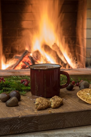 Big red mug with hot chocolate, near cozy fireplace, mulled orange fruit, nuts, in country house, winter vacation, vertical.の写真素材