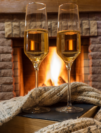 glass of wine, book and warm wool scarf near cozy fireplace in country house, winter vacation.の写真素材