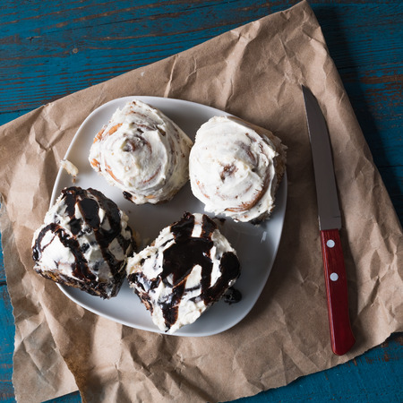 Flat lay of Cinnabons - cinnamon rolls with cream cheese and chocolate, on plate, over brown paper.の写真素材