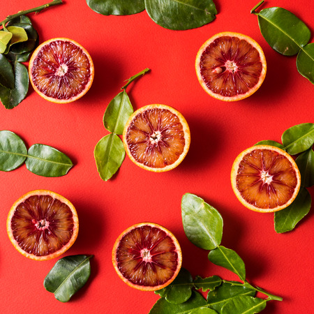 Healthy eating concept. Pattern with raw fresh red orange fruit with green leaves. Flat lay, over red background.の写真素材