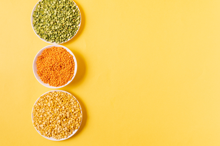 Top view of assortment of peas, lentils, beans and legumes over yellow background, with copy space.