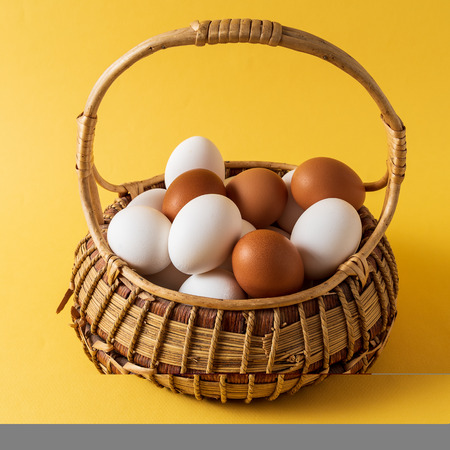 White and blue eggs in a basket over yellow background, front view, vertical image.の写真素材