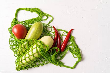 Flat lay Fresh vegetables into the eco Reusable zero waste mesh shopping bag over white background, horizontal orientation.の写真素材