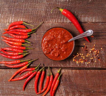 Hot chilli pepper sauce paste harissa, traditional Tunisia, Moroccan, Arabic cuisine adjika ,chili pepper spices and fresh red chilli peppers, over wooden background.の写真素材