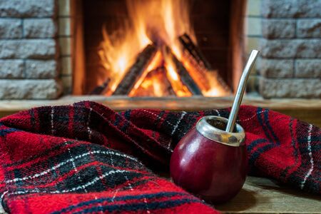 Traditional cup for mate drinking and wool scarf, near cozy fireplace, in country house, hygge, home...