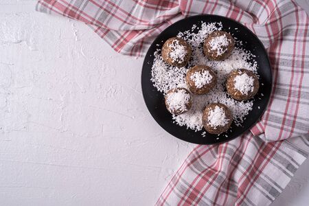 Healthy organic energy balls made with dates, prunes, raisins, peanut, with coconut shavings, in black plate on white background, flat lay.の写真素材