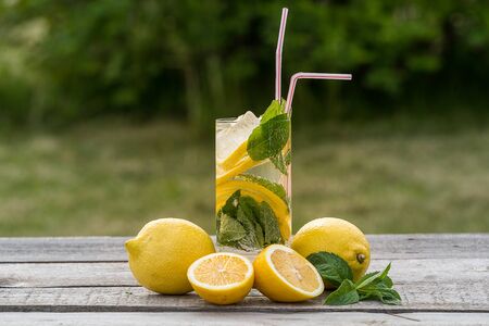 Summer concept. Homemade Lemonade with lemon, mint and ice, in a glass, over old wooden table, outdoor, blurred green background.の写真素材