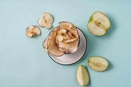Flat lay Dried apple chips in a cup and fresh apples on light blue background.