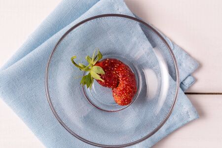 Ugly home grown strawberry on a plate on white wooden background.の写真素材
