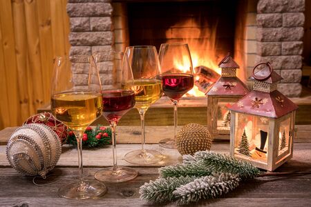 Christmas eve. Glasses of white and red wine, candles and christmas decorations near cozy fireplace, in country house, winter vacation.の写真素材