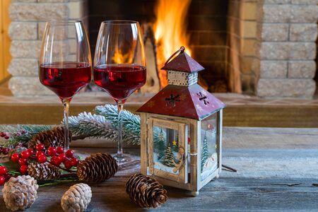 Christmas, New year. Two glasses of red wine, christmas lantern and decorations near cozy fireplace, in country house, winter vacation.の写真素材