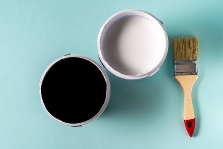Two cans with white and black paint and The brush on blue background. Copy space for your text.