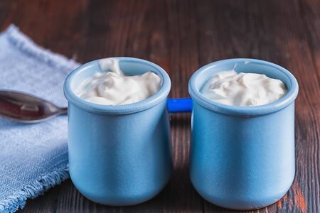 Healthy organic fresh and delicious creamy yogurt in blue ceramic cups on white wooden tabke.