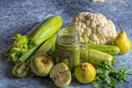 Green healthy smoothie and green vegetables and fruits on gray concrete background. Healthy food and diet concept.の写真素材
