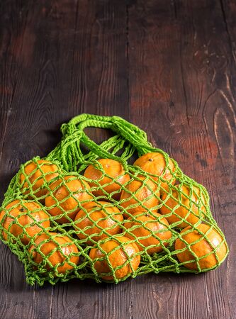 Top view Mesh string shopping bag with fresh oranges from supermarket on brown .の写真素材