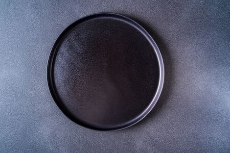 Empty black plate over black table top view, copy space for text.の写真素材