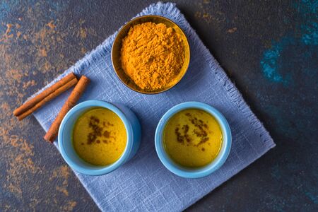 Ayurvedic golden turmeric latte milk made with turmeric and other spices, on wooden background. Healthy medicine drink. Selective focus on background.の写真素材