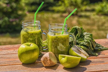 Vegan Green Smoothie With Spinach, apple, celery, kiwi, Brussels sprout, avocado, in glass jars, outdoor over nature backgroundの写真素材