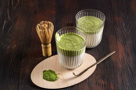 Matcha green tea latte, matcha powder and bamboo whisk on wood background. Top view.