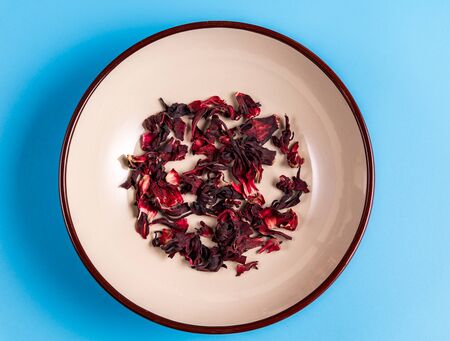Pile of dry hibiscus karkade herbal tea on a plate on blue background, top view.の写真素材