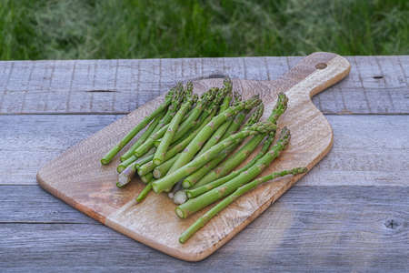 Bunch of fresh green asparagus spears in a cutting board on a rustic wooden table summer outdoor.の写真素材