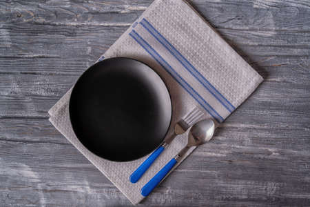 Black plate on wooden table, top view, place for a menu or recipe.