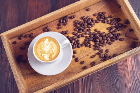 A Cup of latte art coffee and nearby coffee beans in a wooden box on a dark wooden background.の写真素材