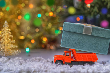 A toy red truck carries a festive box with a Christmas gift on a colorful sparkling bokeh background. The Concept Of A Merry Christmas.の写真素材