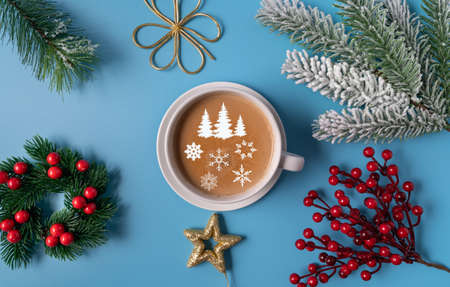 A Cup of coffee with milk on a blue background, and the silhouette of a Christmas tree ans snowflakes on the foam, flat lay, copy space. Christmas concept.の写真素材