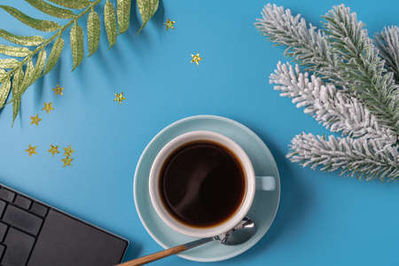 Cup of black coffee, branch of new year tree and keyboard on blue background, flat lay. Christmas...