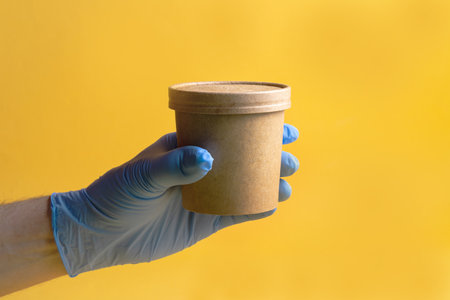 Soup or coffee in a paper disposable Cup for food delivery in the hand of a man in a glove on a...