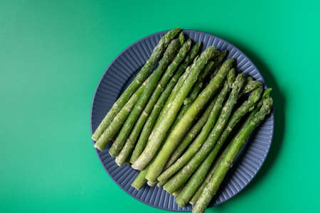 Frozen green asparagus in a black plate on green background, flat lay, top view.の写真素材