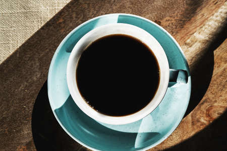 Flat lay black coffee in a cup on cutting board background, sun rise shadows.の写真素材