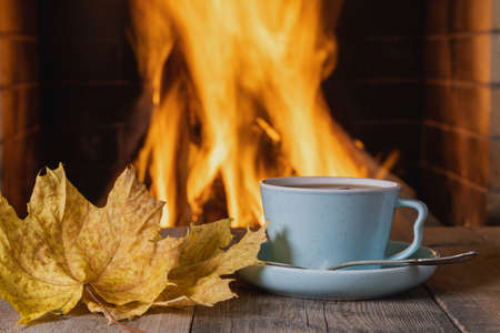 A cup of tea or coffee and autumn leaves near a cozy fireplace, in a country house, autumn or winter holidays,horizontal.の写真素材