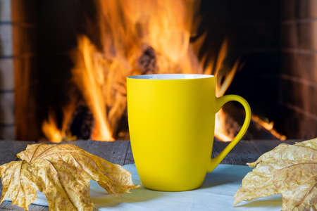 Yellow mug of tea or coffee before a cozy fireplace, in a country house, autumn or winter holidays, horizontal.の写真素材
