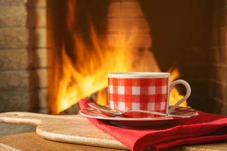 Cup of tea or coffee near a cozy fireplace, in a country house, autumn or winter holidays, horizontal.の写真素材
