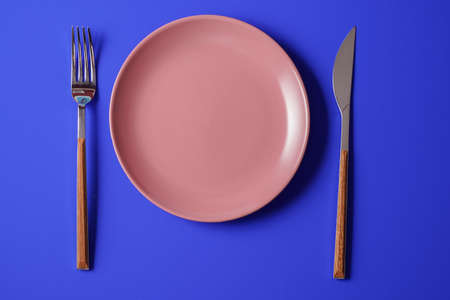 Minimalism style. Empty plate and a cutlery set on blue paper background.