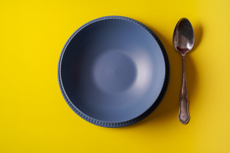 Minimalism style. Empty black plate and a cutlery set on yellow paper background, flat lay.の写真素材