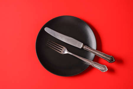 Minimalism style. Empty black plate and a cutlery set on red paper background.の写真素材