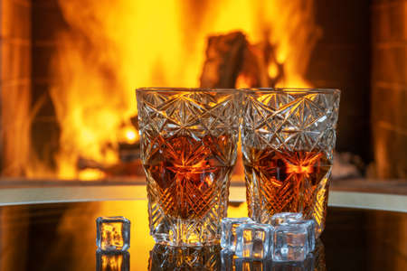 Two glasses of whiskey with ice on a background of a burning fireplace.の写真素材