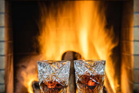 Two glasses of whiskey with ice on a background of a burning fireplace.の写真素材