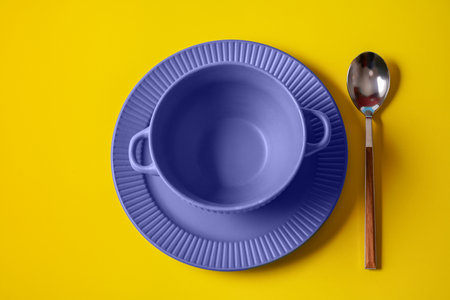 Empty plate of Very Peri color - color of the year 2022 and spoon over yellow color background.の写真素材
